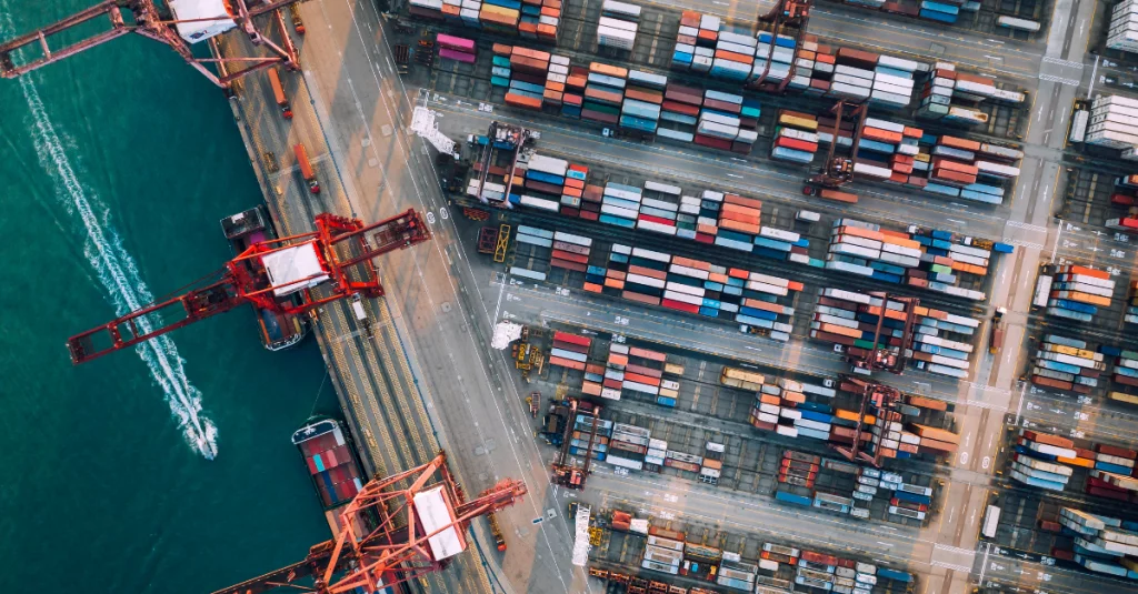 Vista aérea de terminal portuário com contêineres organizados e navio de carga, ilustrando as etapas do comércio exterior para o blog: por que importar parece complicado